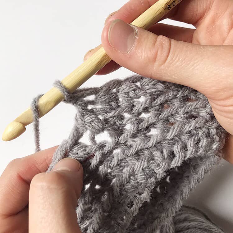 A person creating a pattern using a wooden crochet hook.