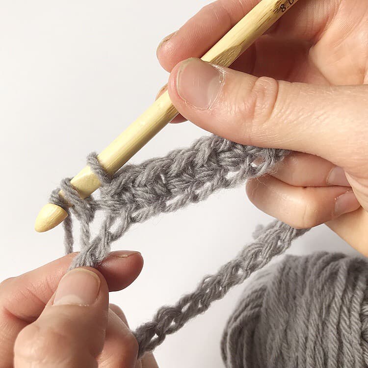 A person creating a crochet pattern with a wooden crochet hook.