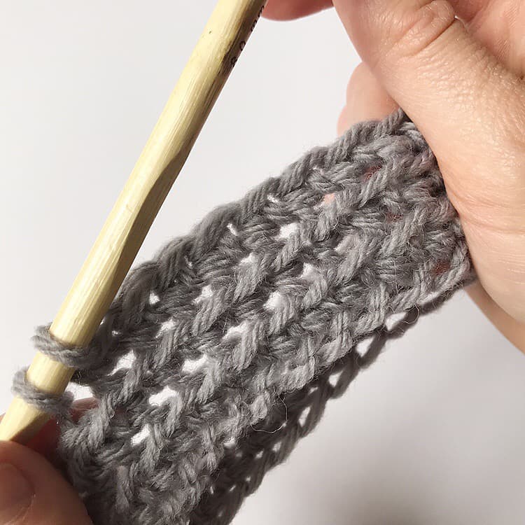 A person using a crochet hook to knit a pattern.