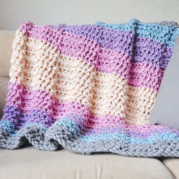 A crocheted afghan with a beautiful pattern sitting on top of a couch.