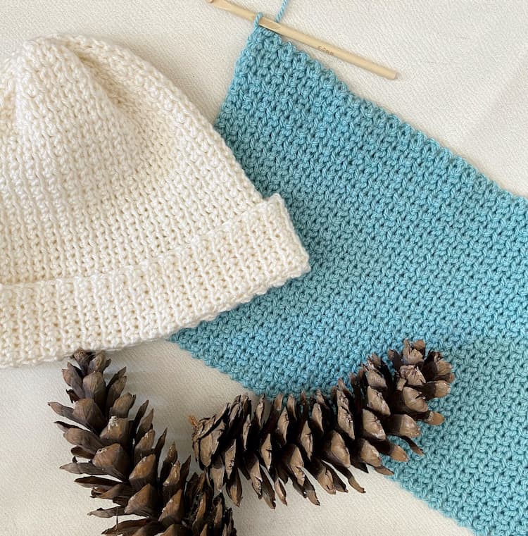 cream crochet beanie hat, crochet hook and fabric with pine cones