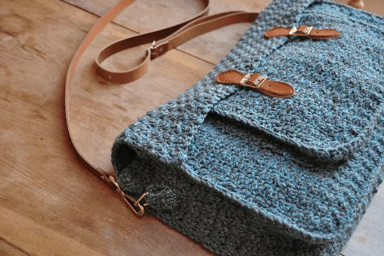 Quotidian Crochet Satchel una bolsa de mensajero con correas de cuero marrón en crochet sobre una mesa de madera