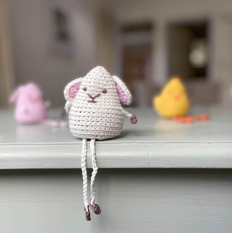 amigurumi crochet lamb toy sitting on edge of shelf