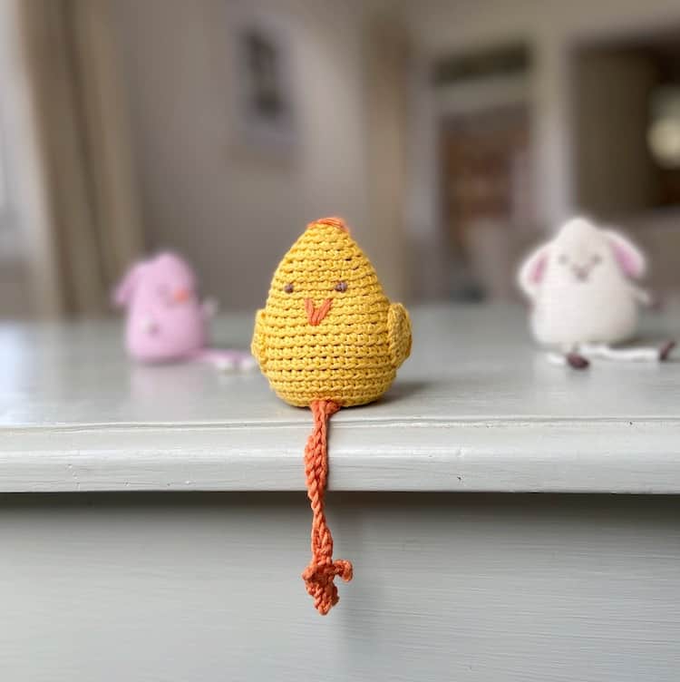 amigurumi crochet chick toy sitting with crossed legs on edge of shelf