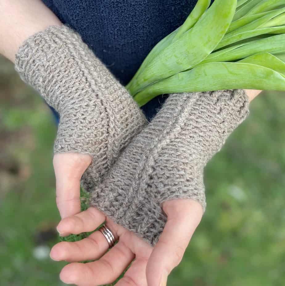 pair of hands wearing crochet hand warmers with palms facing upwards and bunch of tulips tucked in arms