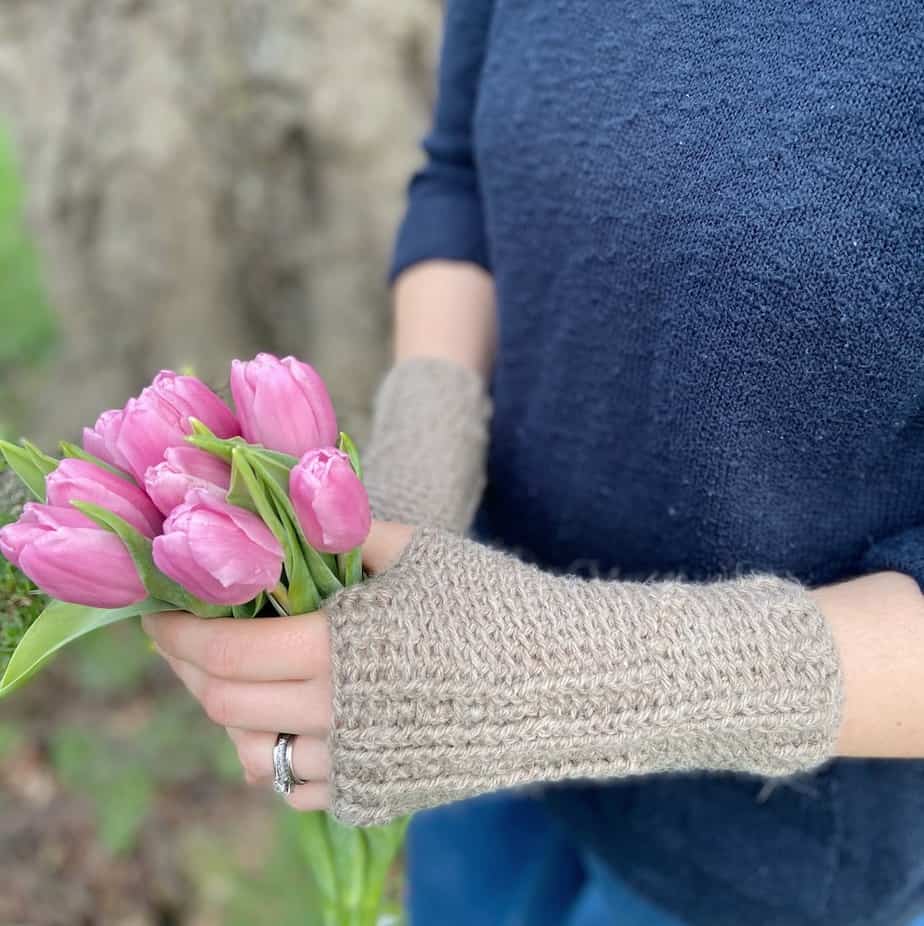Person wearing beige brown crochet hand warmers holding a bunch of pink tulips