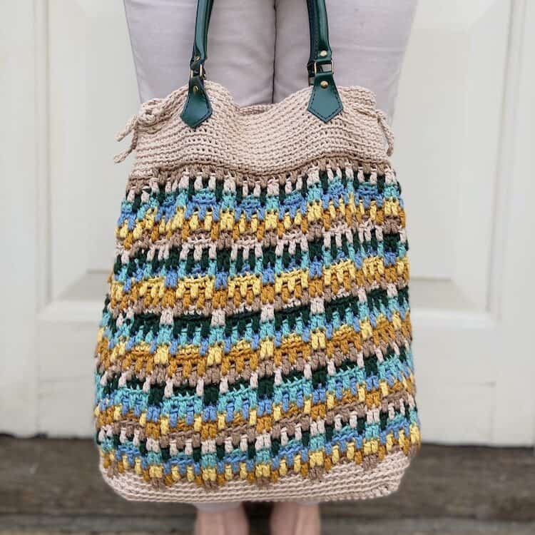 mosaic crochet bag with leather handles held against woman's legs