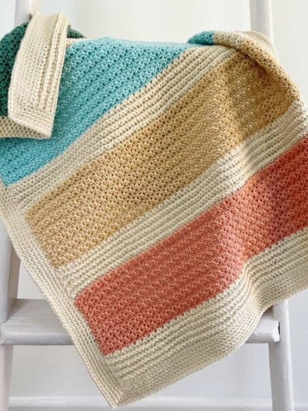 Striped baby blanket crochet pattern in bright colours on a ladder.