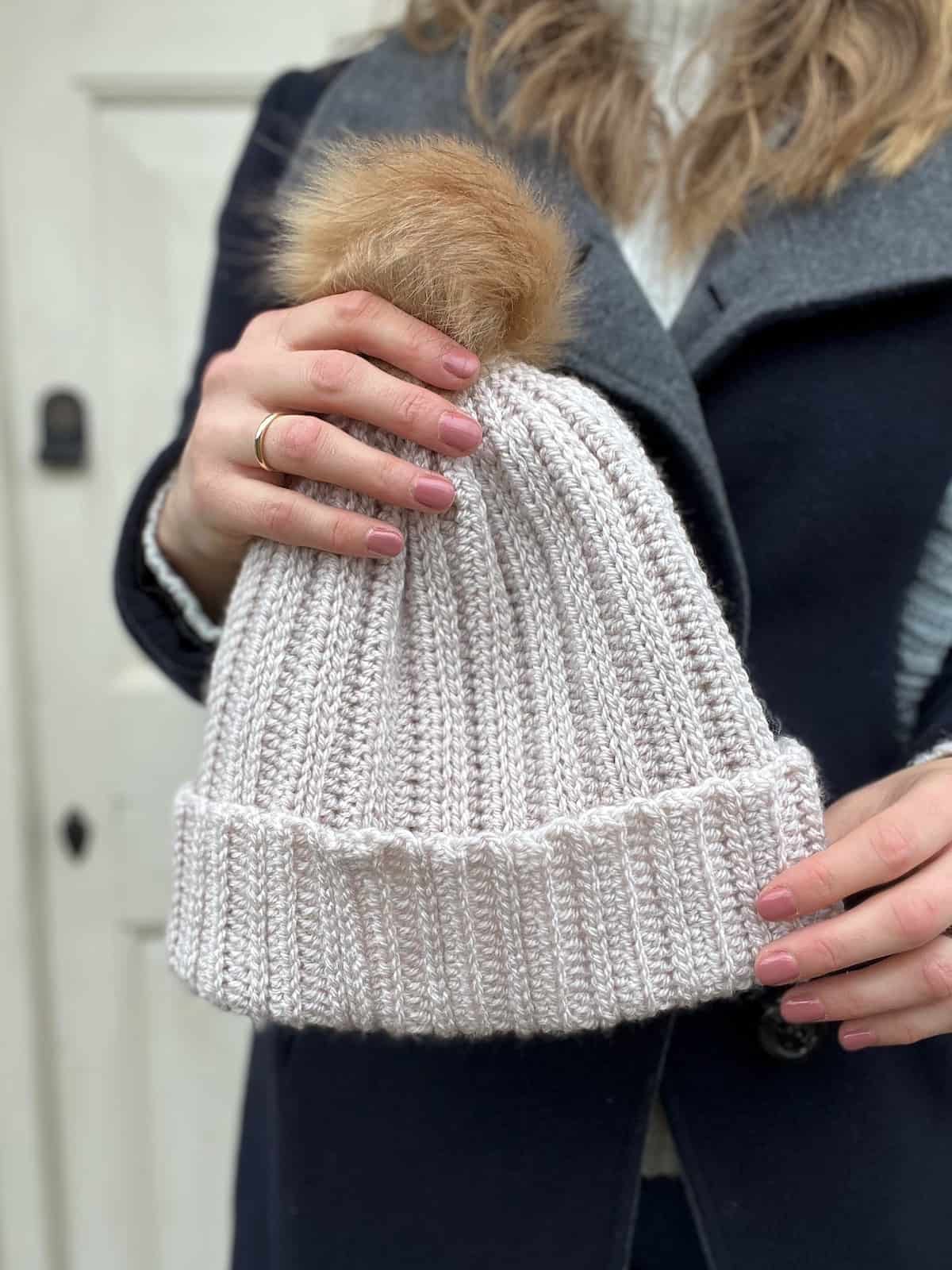 Cream crochet hat with faux fur pom pom on.