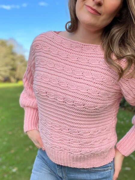 Woman wearing pink crop crochet sweater that has knit look crochet cables in short rows.