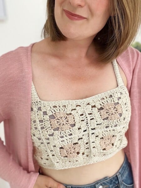 Woman wearing crochet crop top pattern with light pink cardigan over the top.