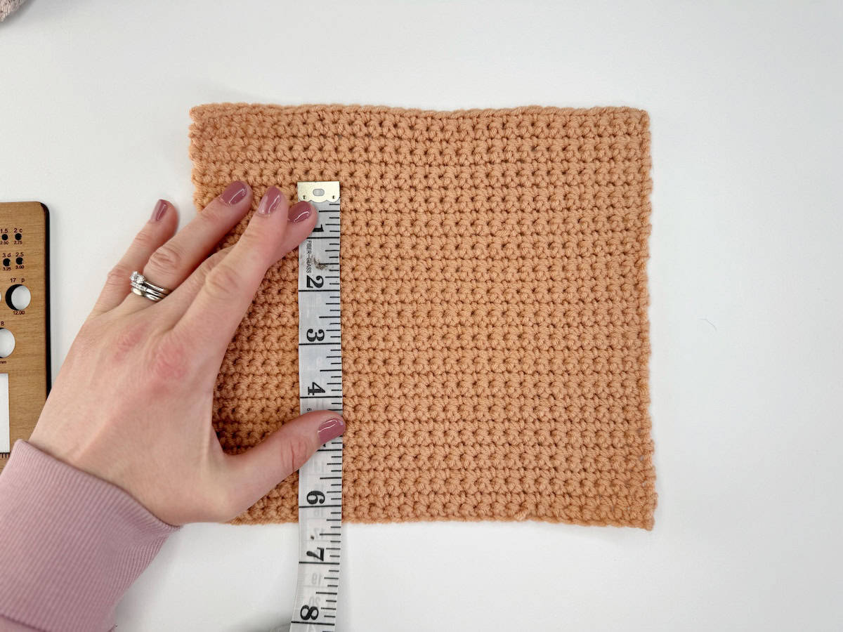 A crochet yarn swatch being measured with a measuring tape to check gauge.