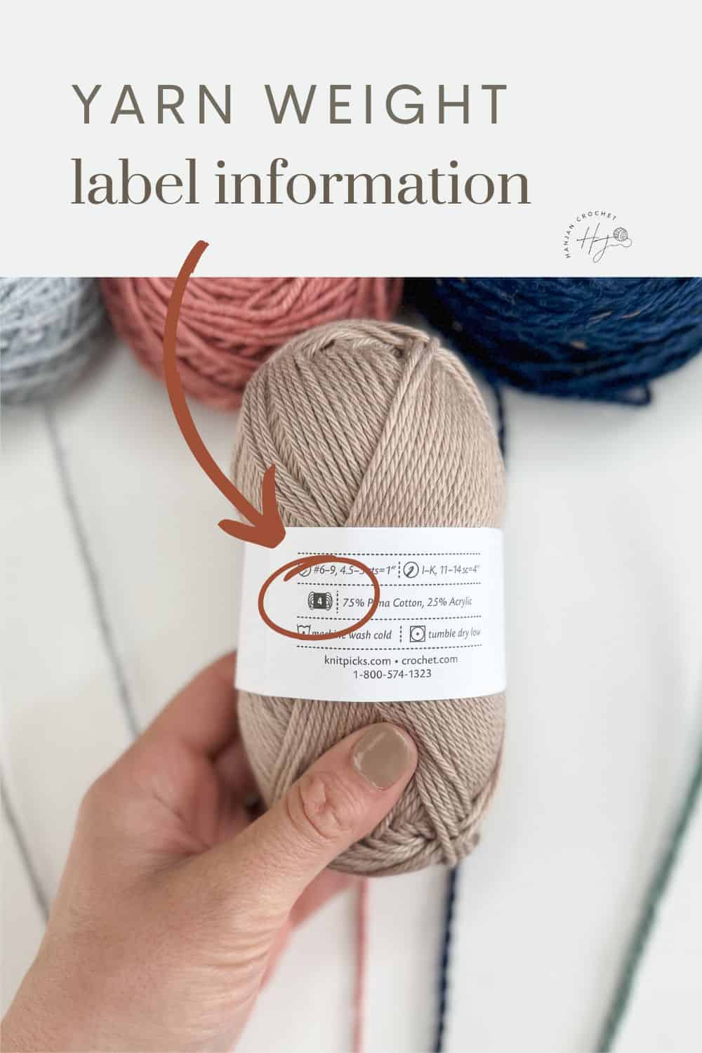 Hand holding a ball of yarn with a label indicating yarn weight and washing instructions. The background includes four other colorful balls of yarn, with a handy yarn weight chart subtly visible at the edge for easy reference.