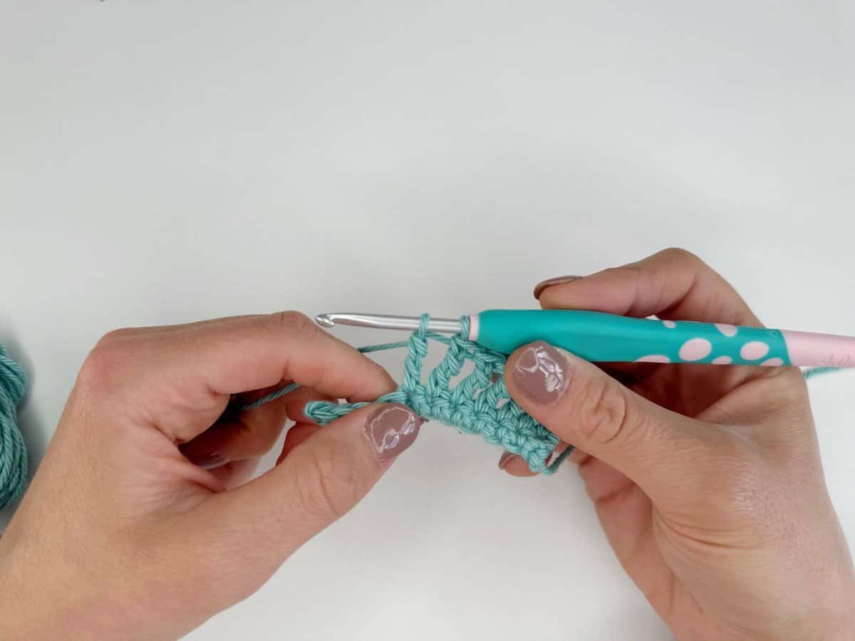 Hands holding a crochet hook with blue yarn, working on long crochet stitches in a beautiful project.