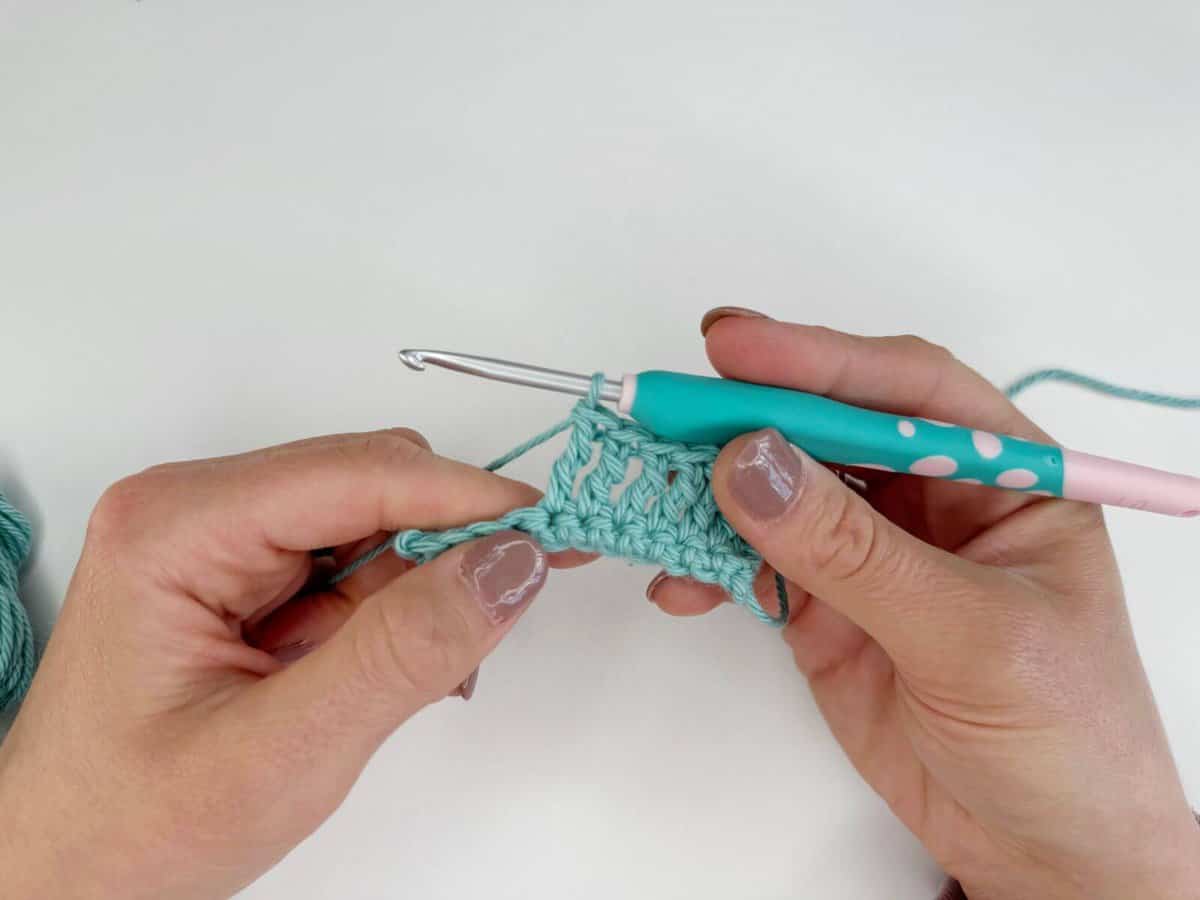 Person crocheting a teal yarn with a light blue crochet hook, crafting long crochet stitches.