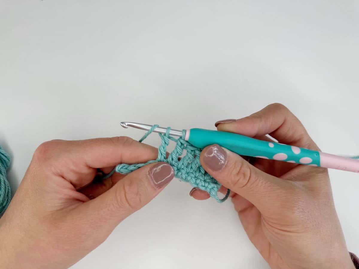 Hands holding a crochet hook and working with light blue yarn, creating long crochet stitches on an intricate project.