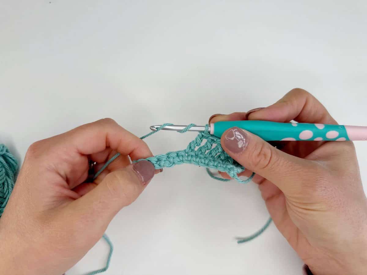 Hands holding a crochet hook and working with light blue yarn, skillfully creating long crochet stitches.