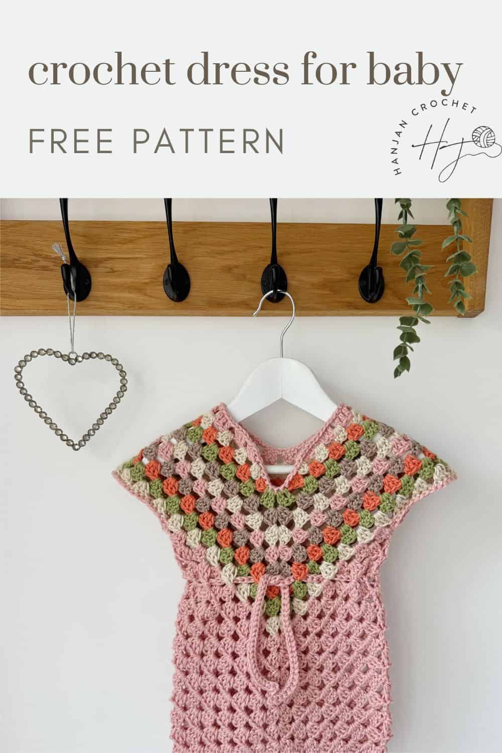 A pink and multicolored crocheted baby dress hangs on a wooden hook rack. Text above reads "crochet dress pattern for baby" and "FREE PATTERN," with a logo in the bottom right corner.