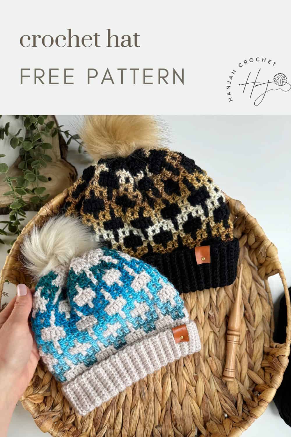 Two crochet hats with pom-poms rest in a basket. One features a mosaic design in blue and white, while the other is in black and brown. A hand holds the blue hat. Text reads: "crochet hat free pattern.