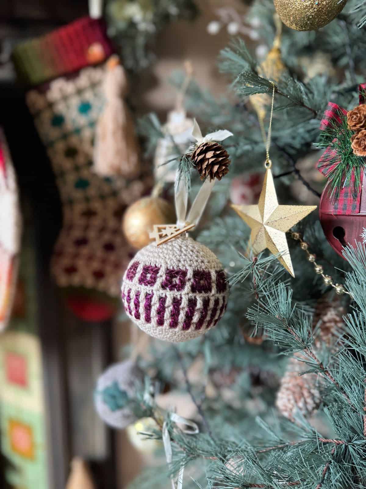 Crocheted Christmas ornaments, including a white and burgundy ball and a gold star, embellish the festive tree. With crochet tree decorations and stockings in the background, it's a scene of holiday charm.