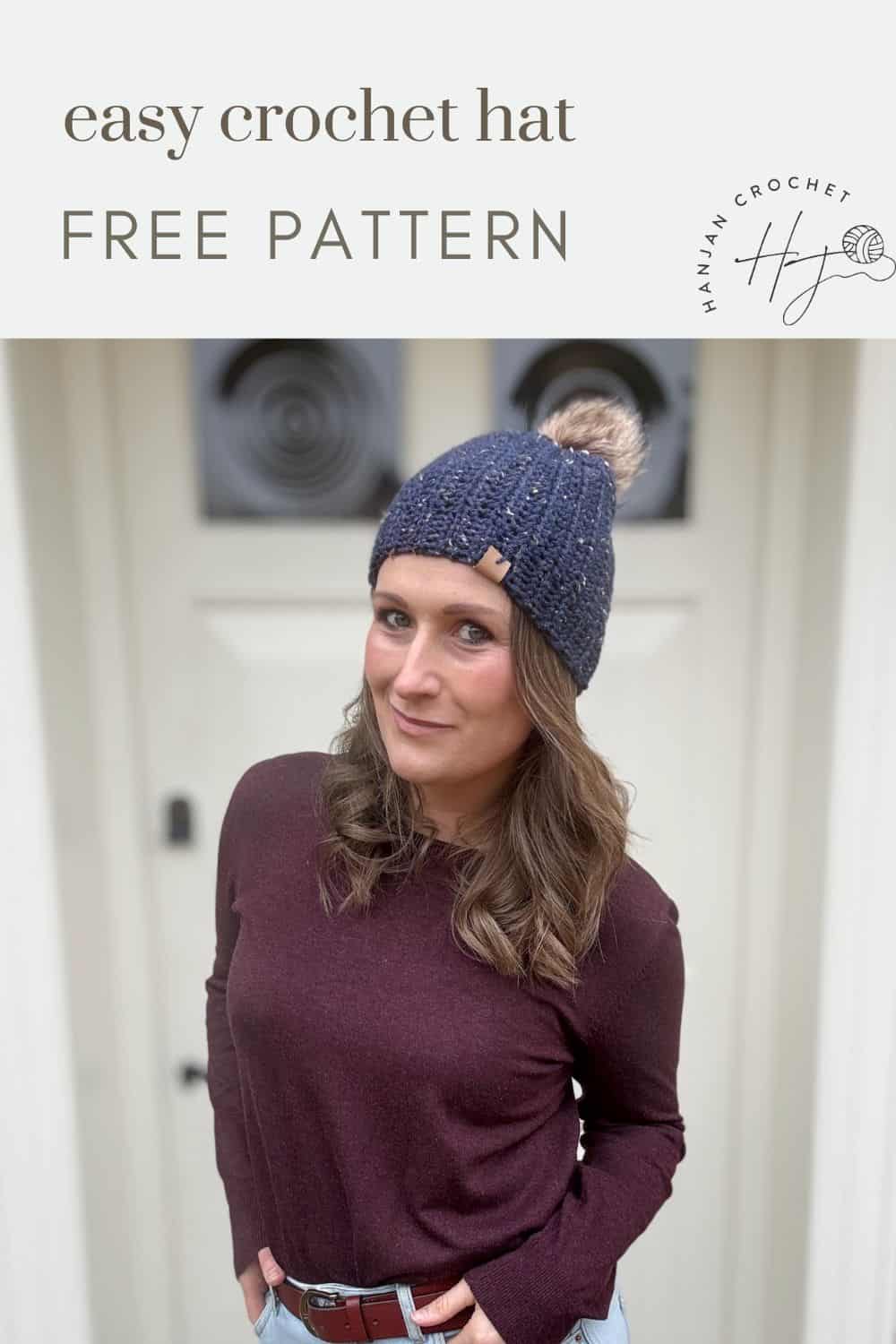 A woman sports a blue crochet hat with a pom-pom as she stands before a white door, showcasing the easy crochet hat pattern. Text on image reads "Easy Crochet Hat Free Pattern.