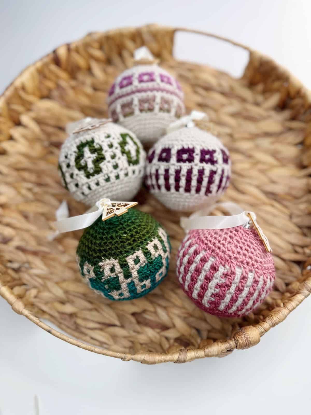 A wicker basket holds five crochet tree decorations in various colors and patterns, including green, pink, purple, and white.