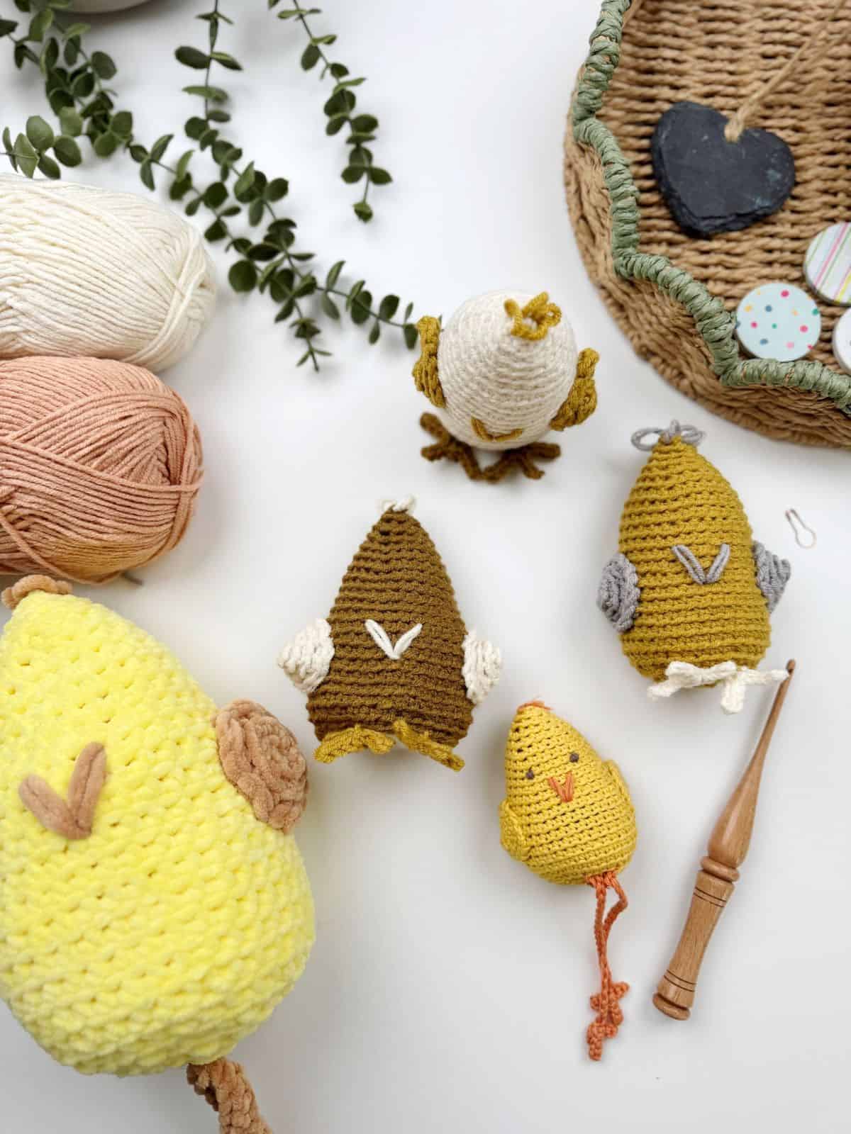 Crocheted chicken toys, crafted with a delightful crochet chicken pattern, display an array of colors on a white surface. They are surrounded by vibrant yarn balls, a woven basket, and a wooden crochet hook.