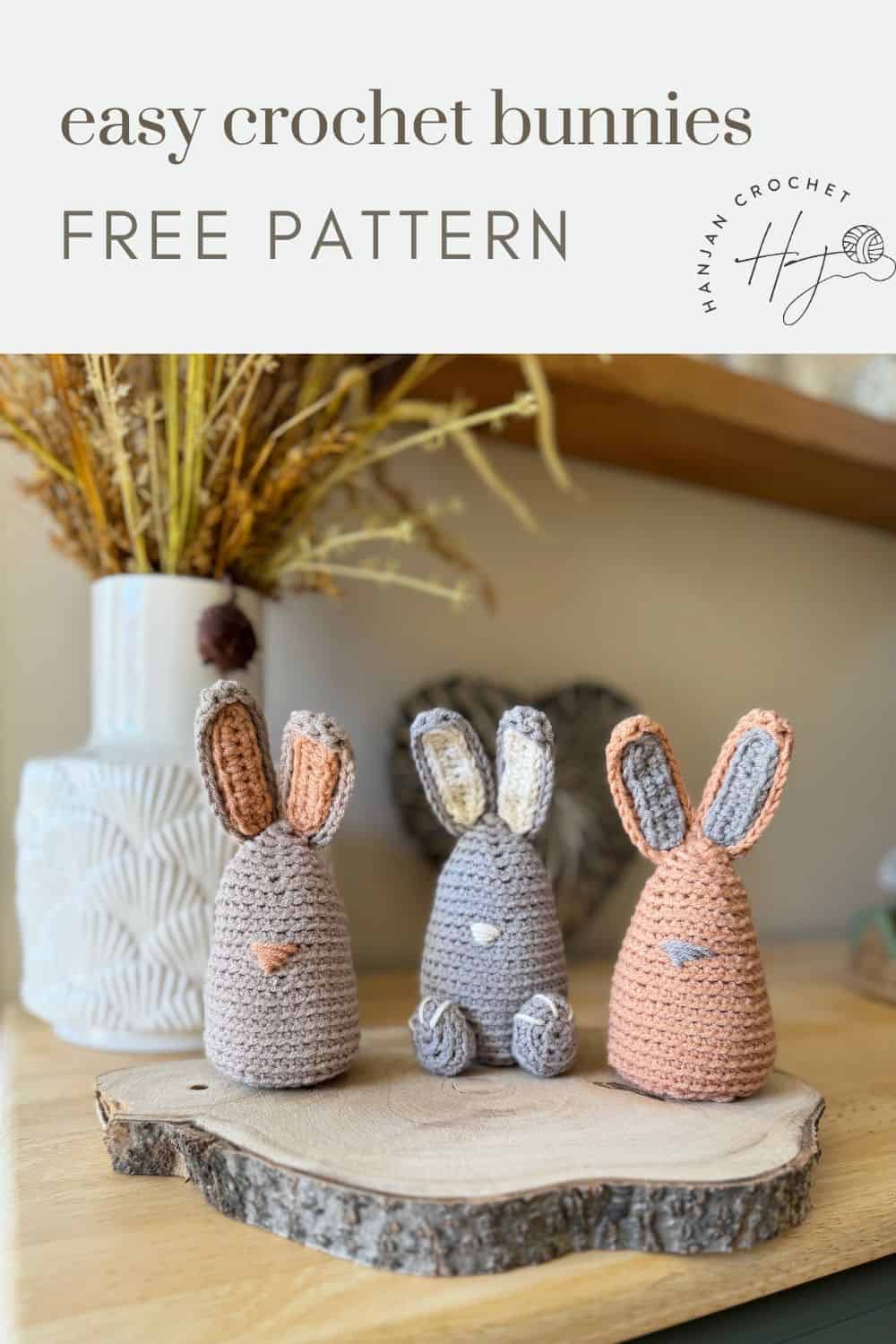 Three crocheted bunnies, two gray and one beige, sit charmingly on a wooden slice with decorative plants in the background. Text reads: "easy crochet bunny pattern FREE PATTERN.