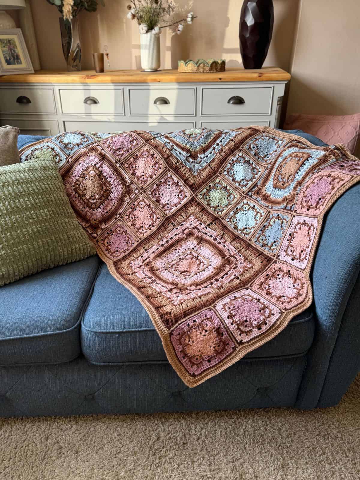 Crocheted multicolored afghan with intricate patterns draped over a blue sofa, accompanied by a green cushion.